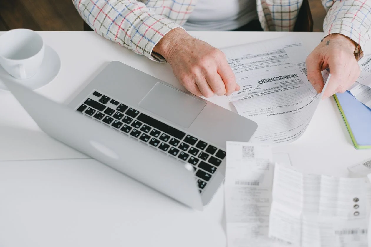 Automate Business Tasks With AI - Person sorting receipts and paperwork by hand with a laptop